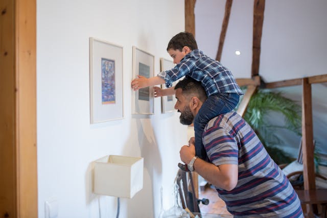 A parent and child hanging photos on a wall together